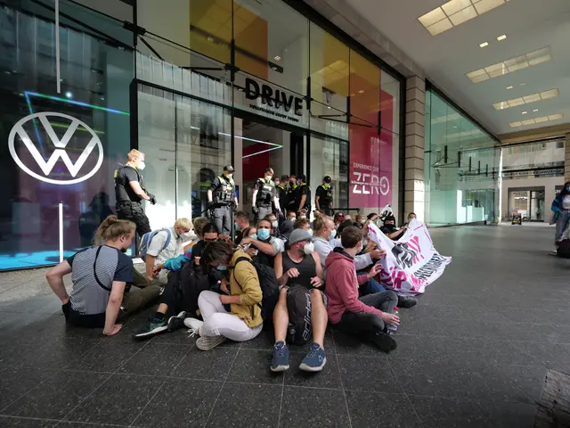 The image shows a group of people sitting on the ground in front of a Volkswagen dealership, with...