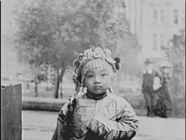 The image shows an old black and white photo of a little girl walking down the street, holding...