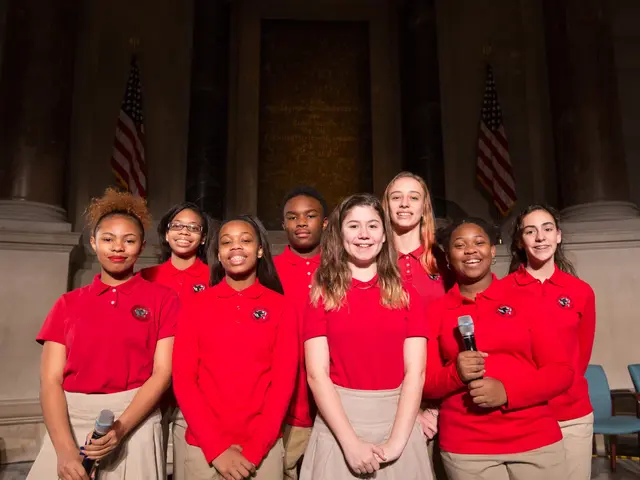 The image shows a group of young women in red shirts standing next to each other, smiling and...