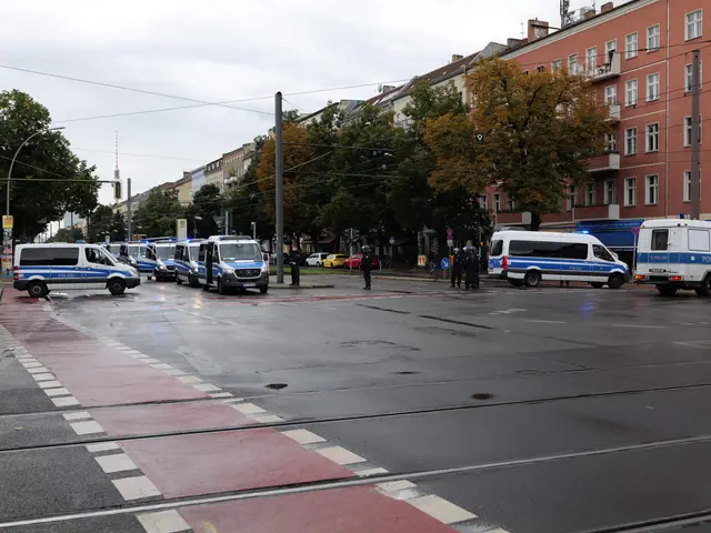 The image shows a street with a group of police cars parked on the side of it. There are people...
