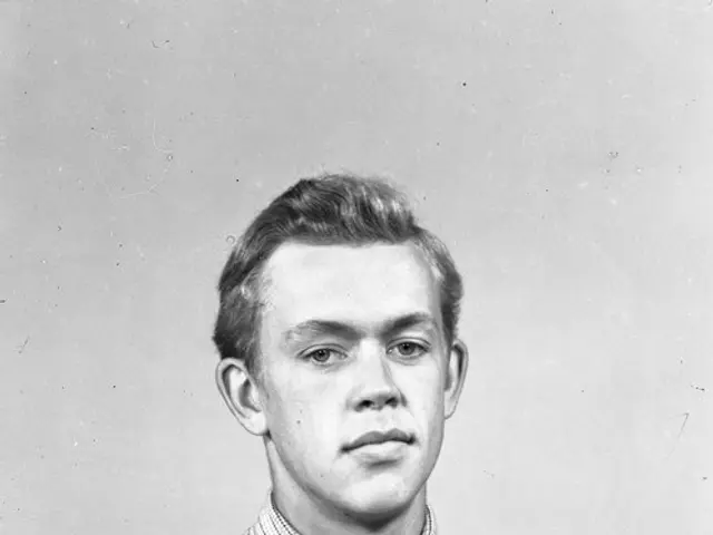 The image shows a black and white photo of a man wearing a shirt and tie, with a watch on his...