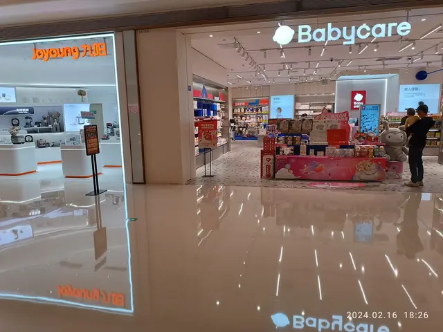 The image shows a babycare store in the middle of a shopping mall, with a group of people standing...