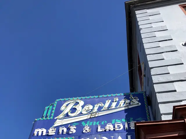 The image shows a building with a blue and white sign hanging from the side of it. The sign reads...