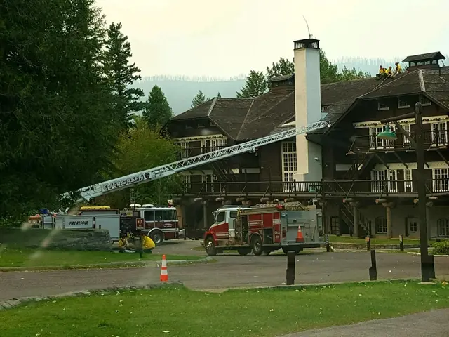 The image shows a fire truck parked in front of a large building with windows, railings, pillars...