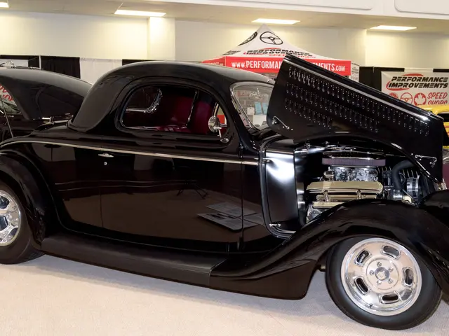 The image shows a black car parked in a showroom with its hood open, surrounded by other cars on...