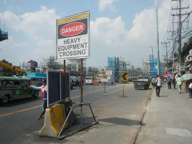 The image shows a busy street with a sign that reads "Danger Heavy Equipment Crossing" on the side...