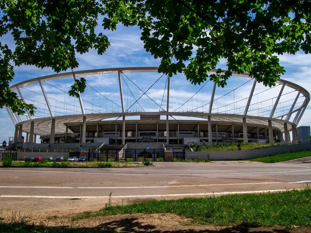 The image shows the Olympic Stadium in London, England. It is a large stadium with a road in front...