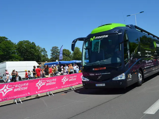 The image shows a black and green bus driving down a street next to a crowd of people, some of whom...
