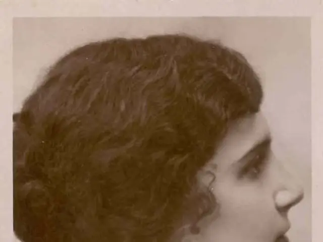 The image shows an old black and white photo of a woman with short hair. At the bottom of the...