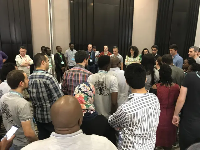 The image shows a group of people standing in front of a crowd of people, some of whom are holding...