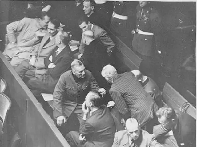 The image shows a group of men sitting in a courtroom, with Adolf Hitler in the center. He is...