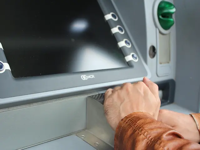 The image shows a person using an ATM machine with their hand on the screen, indicating that they...