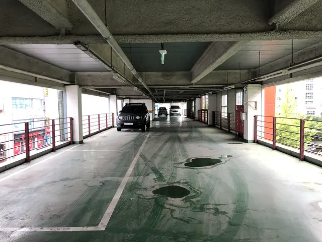 The image shows a parking garage with cars parked in it, surrounded by railings, pillars, lights,...
