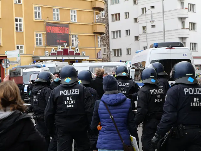 The image shows a group of police officers standing in front of a crowd of people wearing helmets...