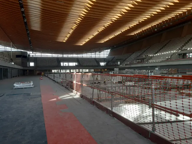 The image shows a large stadium with a lot of construction equipment, including a net fence on the...