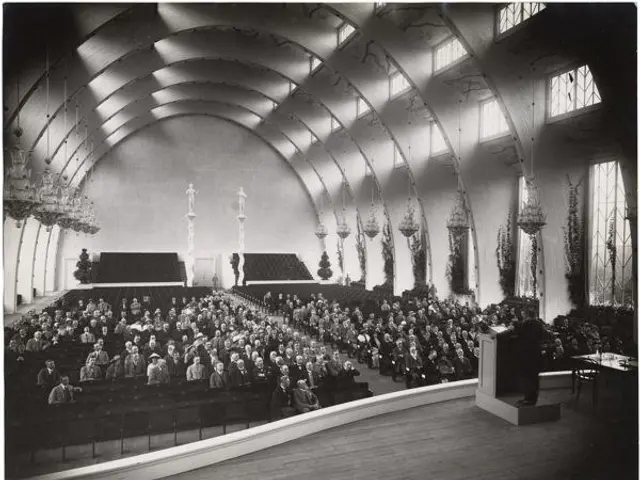 The image shows a large group of people sitting in a church, with a podium in front of them. On the...