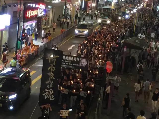 The image shows a large group of people walking down a street at night, illuminated by street...