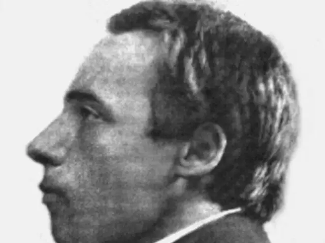 The image shows a black and white photo of a man in a suit, believed to be the first man to be...
