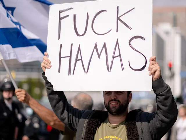 The image shows a man holding a sign that reads "Fuck Hamas" in front of a crowd of people, some of...