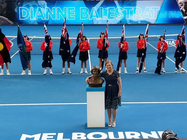 The image shows a woman standing at a podium in front of a crowd of people, some of whom are...