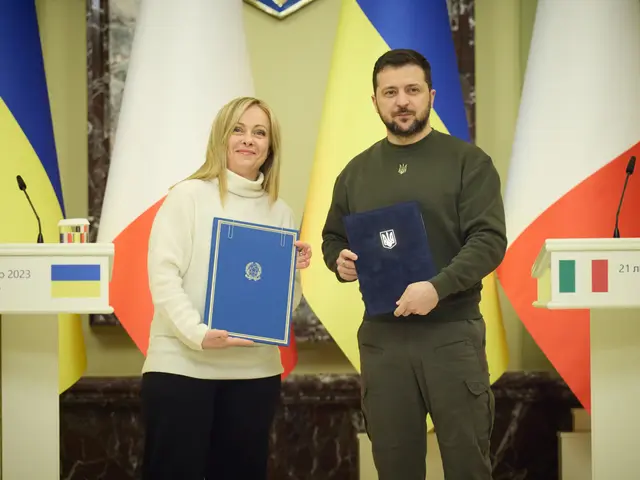 The image shows a man and woman standing next to each other in front of flags, both of them smiling...