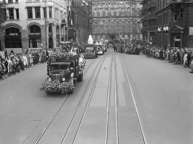 The image shows a black and white photo of a parade on a city street. There are several vehicles on...
