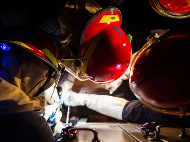 The image shows a group of firefighters wearing helmets and gloves, working on a fire truck in a...