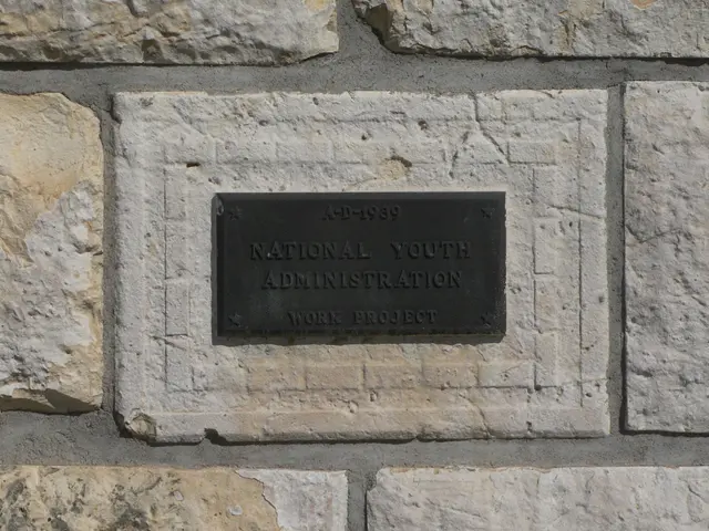 The image shows a stone wall with a plaque on it that reads "National Youth Administration". The...