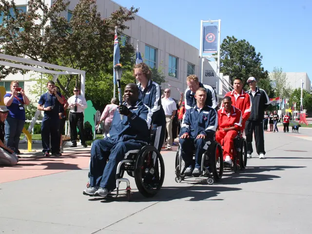 The image shows a group of people in wheelchairs walking down a street lined with trees and...
