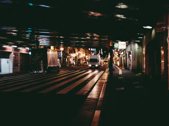 The image shows a city street at night with vehicles on the road, buildings on either side, lights...