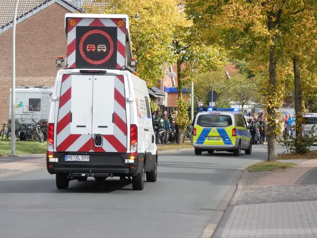 The image shows an ambulance driving down a street lined with trees and buildings, with a group of...