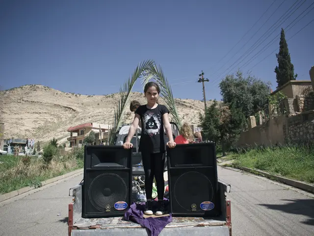 The image shows a young girl standing on top of a truck with two speakers in the back. She is...