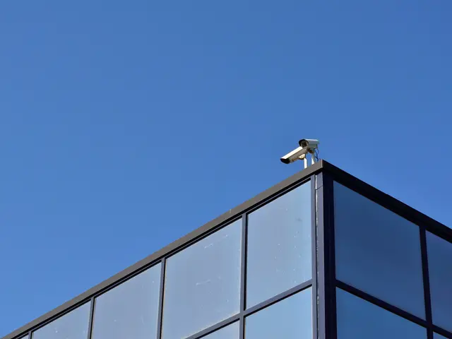 The image shows a security camera mounted on the side of a building, with a clear blue sky in the...