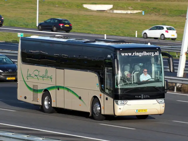 The image shows a coach bus driving down a highway next to a car. There are people inside the bus,...