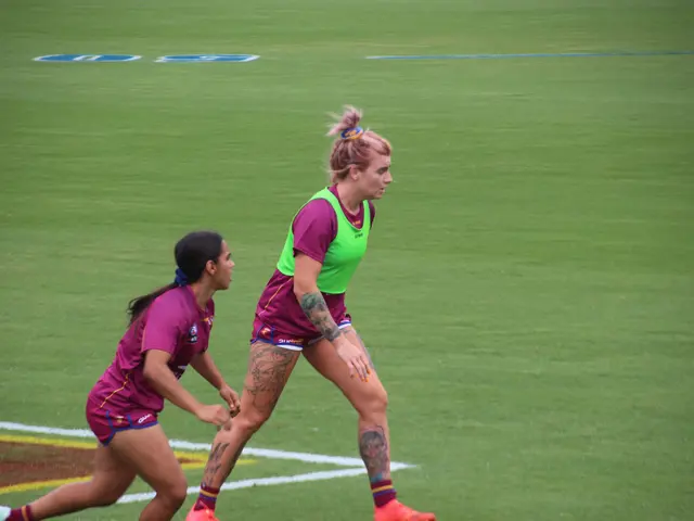 The image shows two women playing a game of soccer on a field. They are both wearing sports attire,...