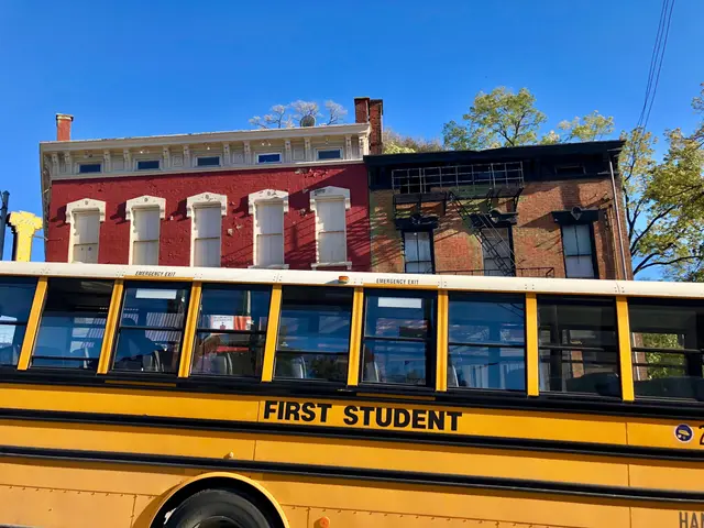 The image shows a yellow school bus parked in front of a red brick building. The bus has the words...