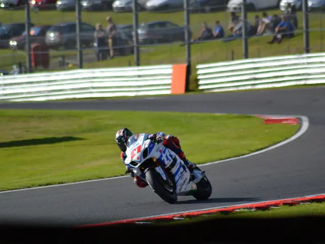 The image shows a person wearing a helmet and riding a motorcycle on a race track. The track is...