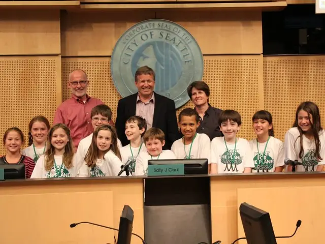 The image shows a group of children and adults standing in front of a podium, smiling and posing...