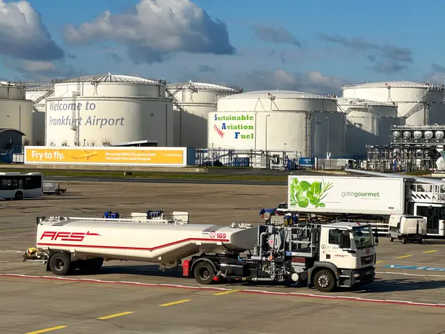 The image shows a large tanker truck parked in front of a large building at Frankfurt Airport. The...