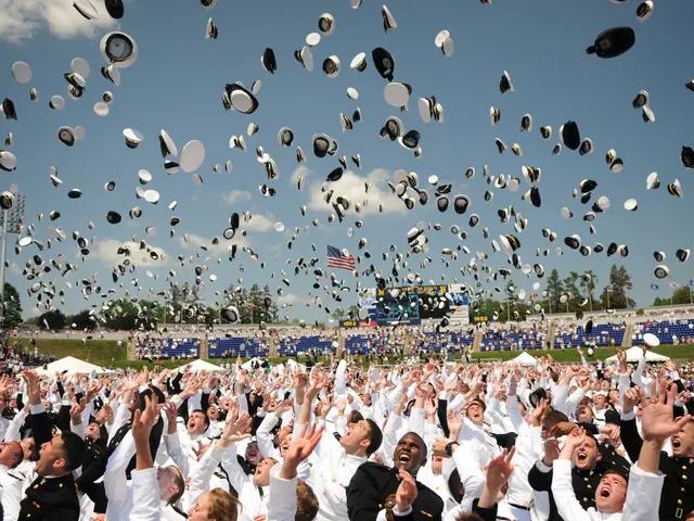 The image shows a large group of people in white graduation caps and gowns throwing their hats in...