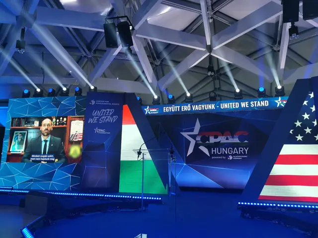 The image shows a stage set up for a political event with an American flag on it. There is a person...