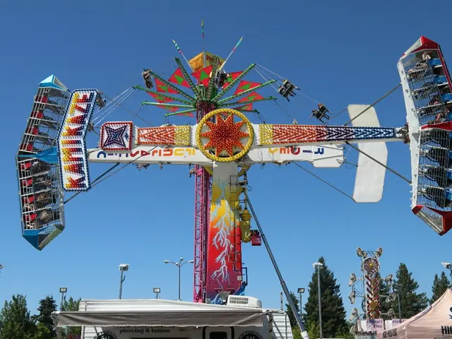 The image shows a carnival ride at a fair with people on it, surrounded by tents, banners, poles,...