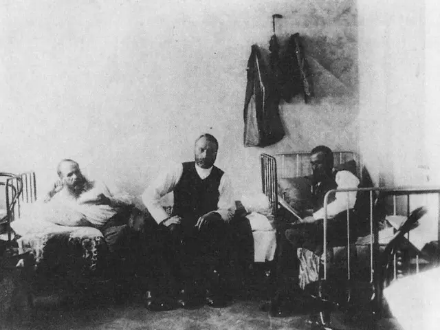 The image shows a black and white photo of three men sitting in a hospital room. The room is filled...