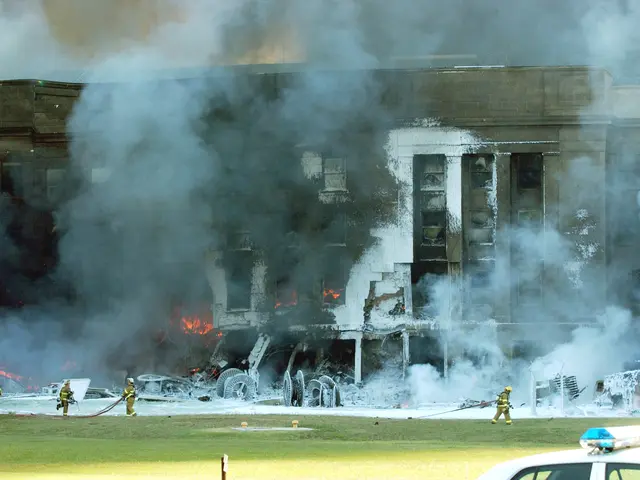 The image shows a large building engulfed in flames and smoke, with firefighters working to put out...