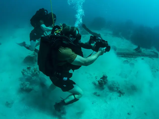 The image shows two scuba divers taking a photo of a shipwreck in the ocean. They are wearing...