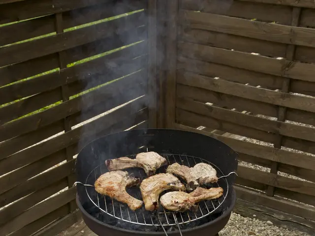 The image shows a barbecue grill with meat cooking on it in the middle of a gravel area, surrounded...