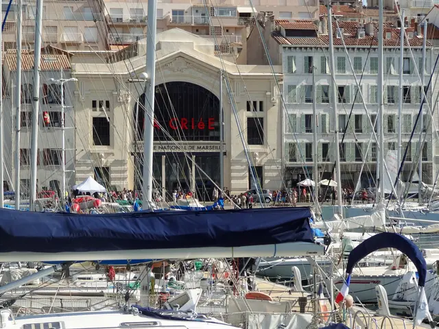 The image shows a marina filled with lots of boats docked in the water, with buildings in the...