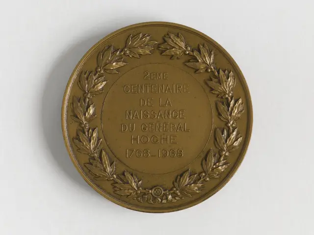 The image shows a gold medal with a laurel wreath on it against a white background. The medal has...