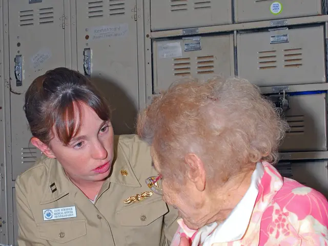 The image shows an older woman sitting in a hospital bed with a nurse standing beside her. On the...