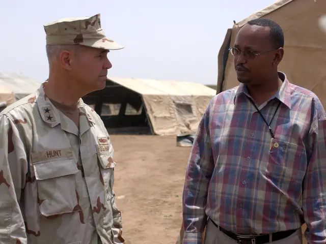 The image shows two men in military uniforms talking to each other in front of a backdrop of tents...